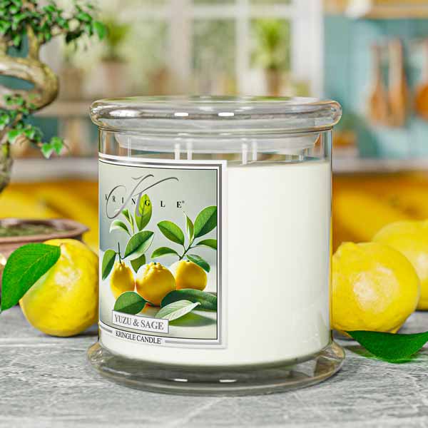 Yuzu & Sage candle in a glass jar with a label, surrounded by lemons and greenery.